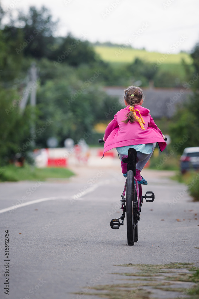 A little random girl from the back, rides a bike down a country road from a hill with no effort. A little random girl from the back, rides a bike down a country road from a hill with no effort.
