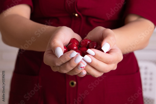  Female hands with white manicure nails holding sweet cherries