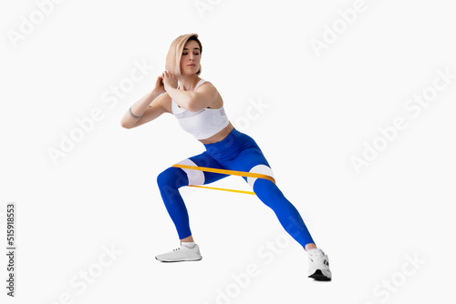 Sexy woman in sportswear using a resistance band in her exercise routine. Young woman performs fitness exercises on white background. Isolate © zamuruev