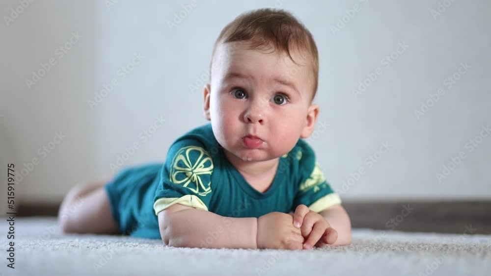 Beautiful Caucasian healthy child lies on the carpet on his belly. Lovely kid looking into camera with his eyes wide-open. Close up. Beautiful Caucasian healthy child lies on the carpet on his belly. Lovely kid looking into camera with his eyes wide-open. Close up.