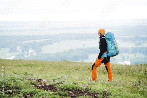 Traveling with a backpack through the mountainous terrain  hiking alone through the valley  a tourist guy in the mountains wore a hat  orange pants.