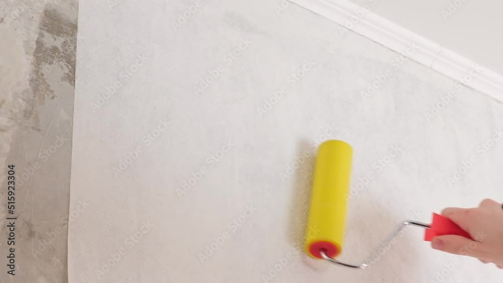 A man rolls out a canvas of white wallpaper with a suture wallpaper yellow roller. Removing air