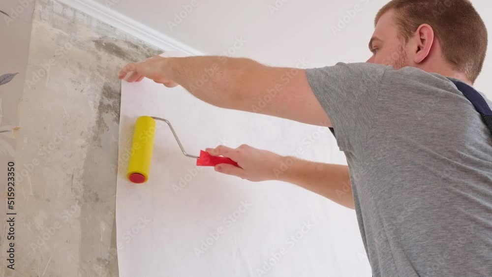 A man rolls out a canvas of white wallpaper with a suture wallpaper