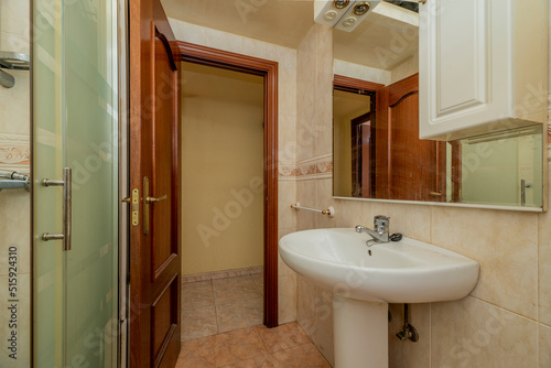 Bathroom with white wood-framed mirror  glass-enclosed shower stall and white porcelain toilets and varnished brown wooden door