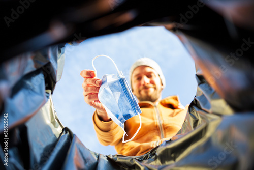 Man smiling throwing a covid surgical mask into a trash can. View from the inside trashcan.