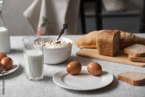the table is covered with a linen tablecloth and on it are natural and healthy products, milk and cottage cheese, bread and boiled chicken eggs