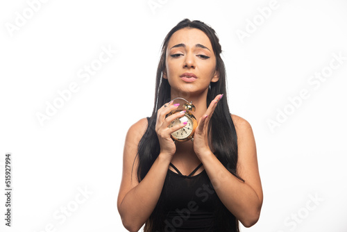 Portrait of young woman posing with an alarm clock on white background