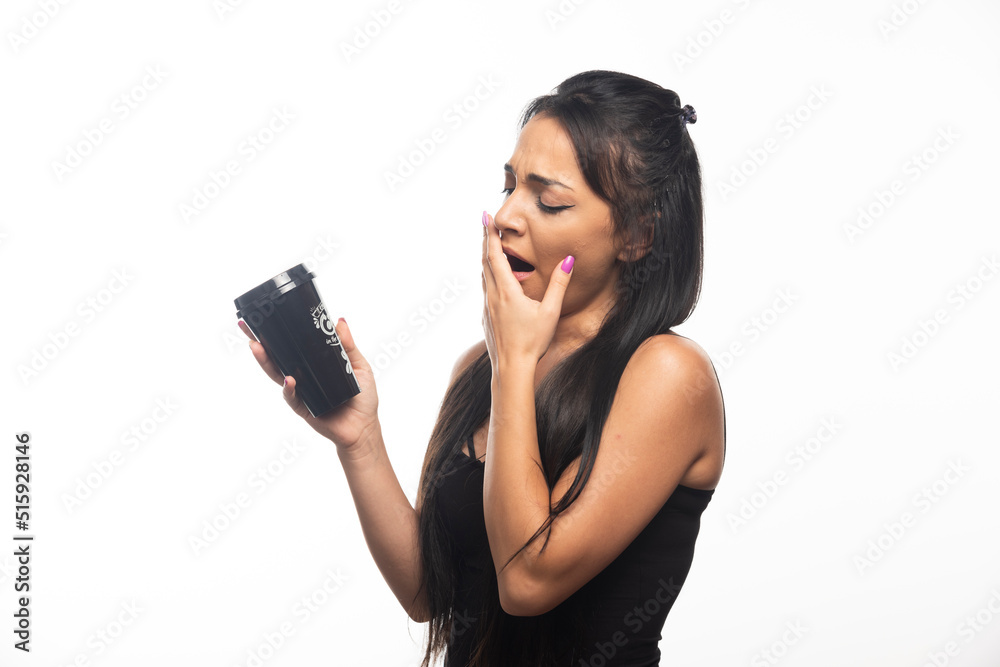 Young woman yawning and holding a cup on white background