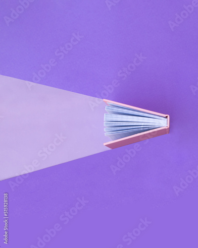 Creative education concept. Minimal composition with book on pastel purple background. Back to school idea. Knowledge and light inspiration.