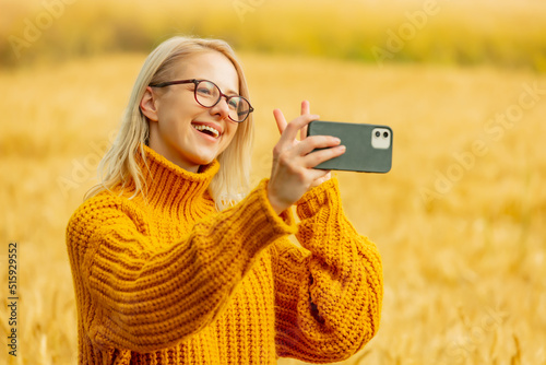 girl in eyeglasses and yellow sweater with mobile phone in wheat field