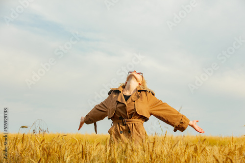 Stylish girl in eyeglasses and cloak in wheat field