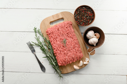 Fresh raw meat or ground chicken meat on a wooden cutting board with thyme, spices and garlic. White wooden background. Top view. Copy space.