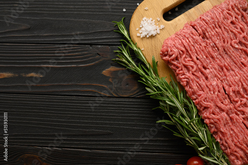 Fresh raw meat or ground chicken meat on a wooden cutting board with thyme, spices and garlic. Rustic wooden background. Top view. Copy space.