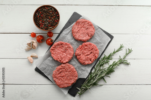 Raw beef burger patties on butcher's wooden board, rosemary and pepper. White background. View from above.