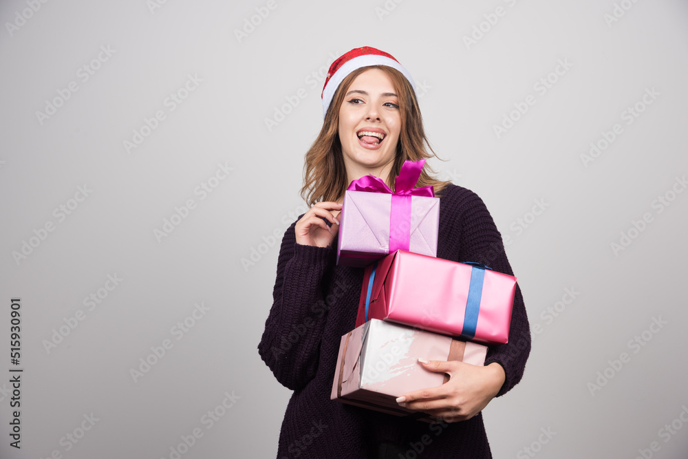 Fototapeta premium Young woman with Santa hat carrying gift boxes presents