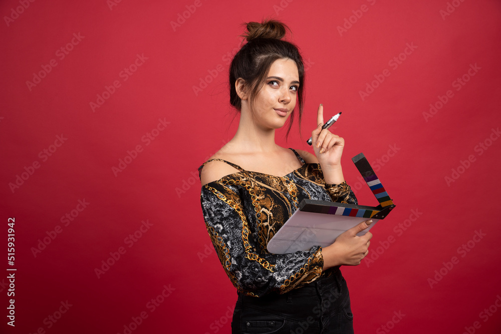Girl with a blank clapper board looking at it, thinking and looks confused Girl with a blank clapper board looking at it, thinking and looks confused