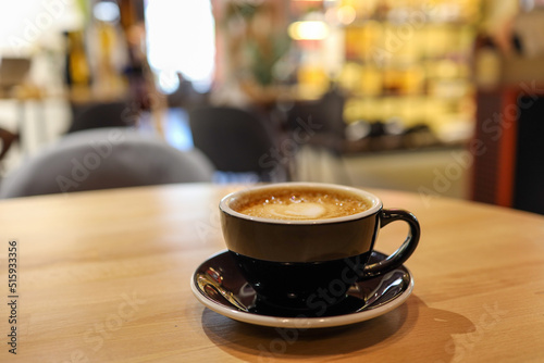 Coffee in black cup on wooden table in cafe with lighting background