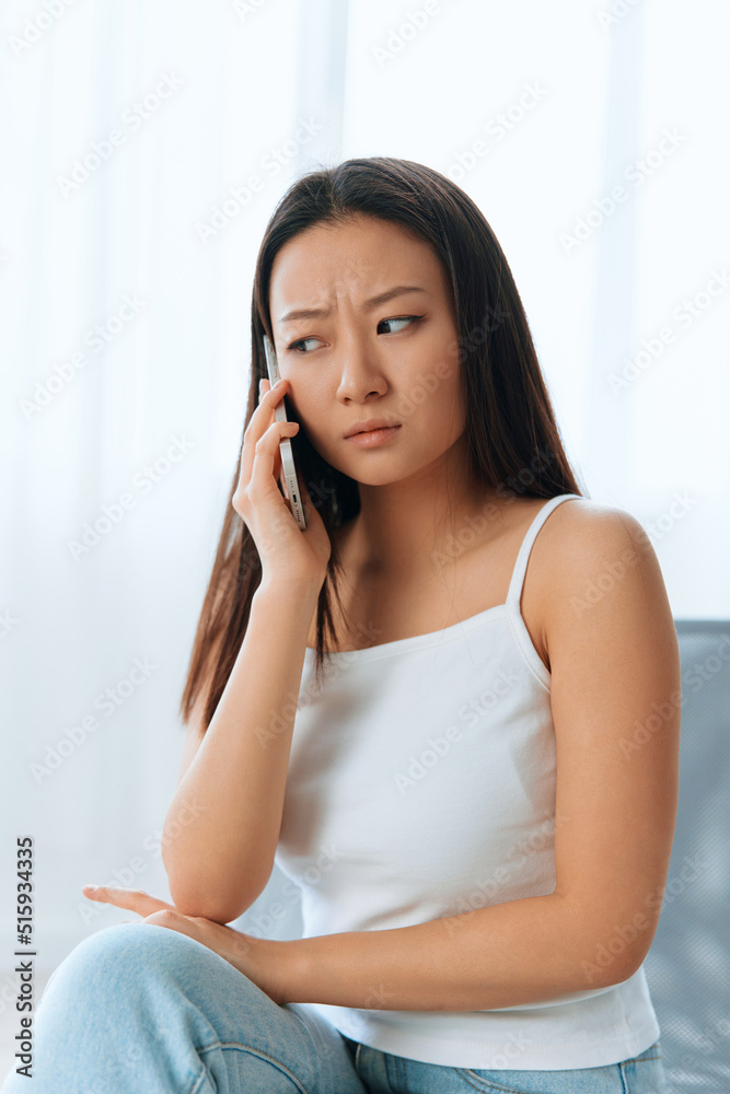 Wary confused attended tanned lovely young Asian woman listen shocked news at call using phone at home interior living room. Distance communication Social media concept. Cool offer Banner Wide angle Wary confused attended tanned lovely young Asian woman listen shocked news at call using phone at home interior living room. Distance communication Social media concept. Cool offer Banner Wide angle