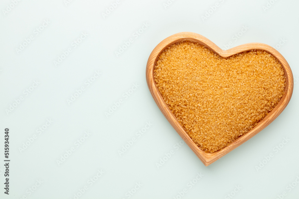 Brown sugar in heart wooden bowl shape on pasttel background.