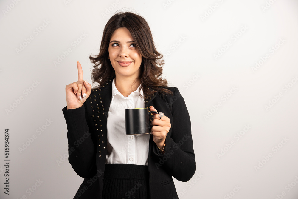 Female office worker pointing at upside while holding tea Female office worker pointing at upside while holding tea