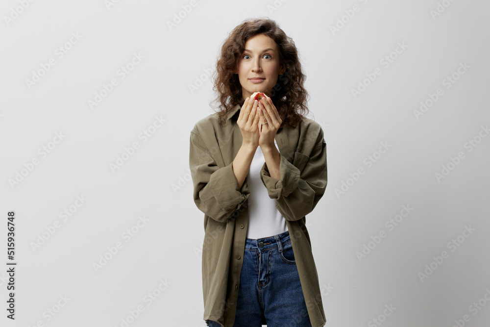 Excited shocked happy funny curly beautiful woman in casual khaki green shirt hold apple looks at camera posing isolated on over white background. Natural Eco-friendly products concept. Copy space Excited shocked happy funny curly beautiful woman in casual khaki green shirt hold apple looks at camera posing isolated on over white background. Natural Eco-friendly products concept. Copy space
