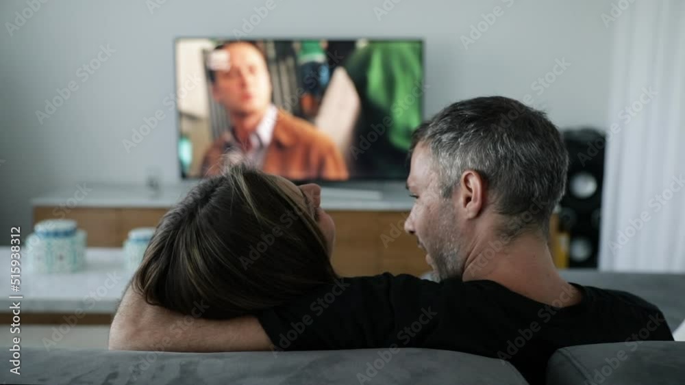 Romantic young couple watching a movie in television while sitting on the sofa. They talk and hug each other. Romantic young couple watching a movie in television while sitting on the sofa. They talk and hug each other.