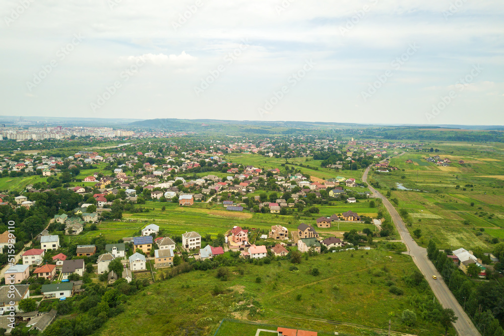 Aerial landscape view of village houses and distant green cultivated agricultural fields with growing crops on bright summer day