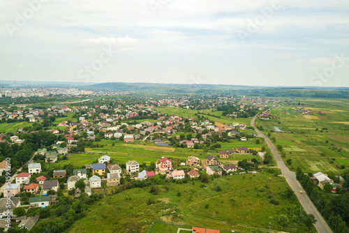 Aerial landscape view of village houses and distant green cultivated agricultural fields with growing crops on bright summer day