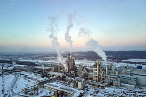 Aerial view of cement factory with high concrete plant structure and tower cranes at industrial production area. Greenhouse gas smoke polluting atmosphere. Manufacture and global industry concept.