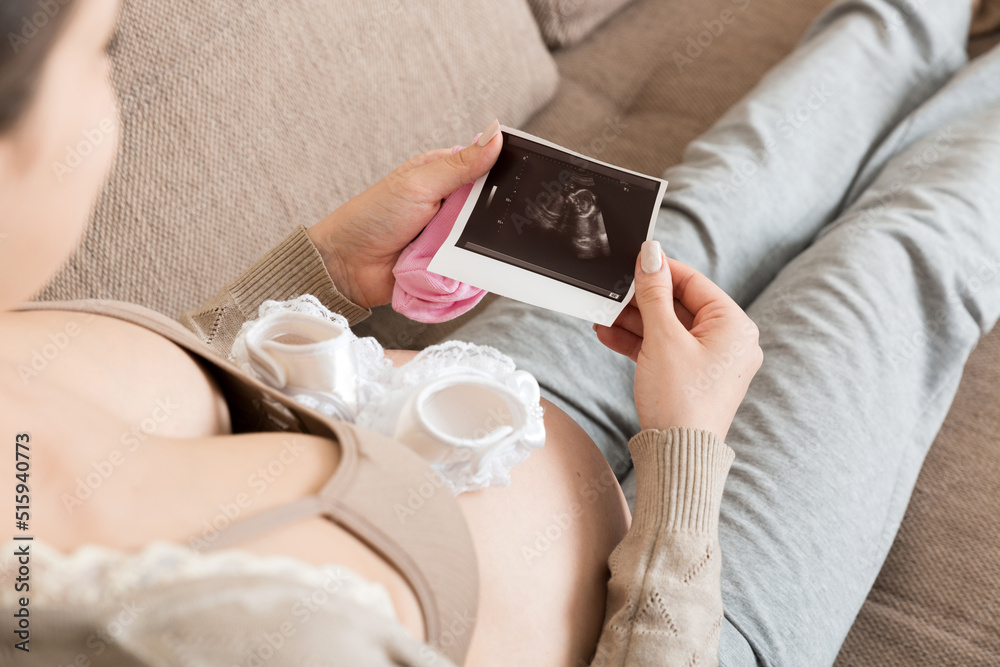 Pregnant Woman sitting on bed and Looking At Ultrasound Scan photo of her Baby. A pregnant female shows her ultrasound report and her unborn baby Pregnant Woman sitting on bed and Looking At Ultrasound Scan photo of her Baby. A pregnant female shows her ultrasound report and her unborn baby