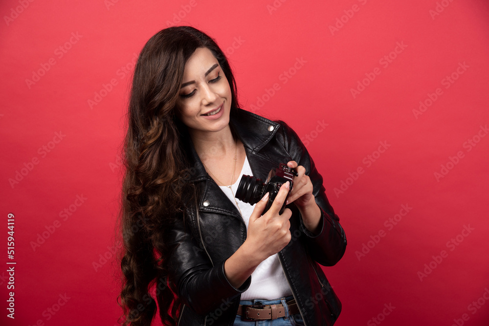 Beautiful woman photographer looking on a photo camera on a red background