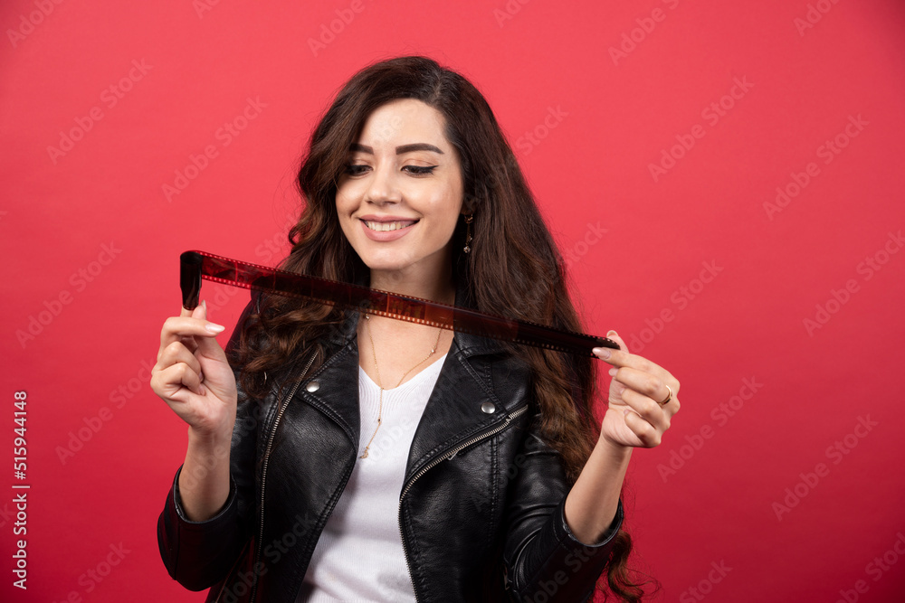 Naklejka premium Young woman looking on a photo tape on a red background