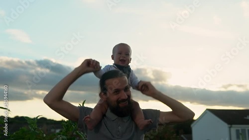Happy Father holding adorable baby boy embracing kissing. Smiling Dad with son playing outside Garden. Family silhouette at sunset. Daddy fly up child as airplane having fun. Parent enjoying with kid