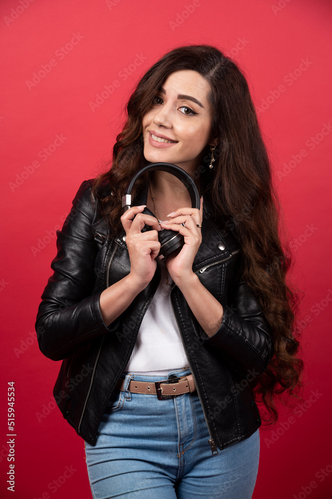 Young woman holding headphones and posing on a red background Young woman holding headphones and posing on a red background