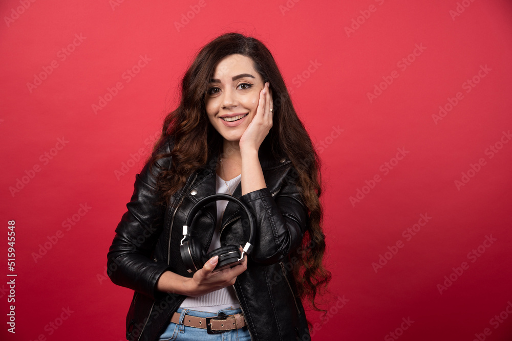 Young woman holding headphones and posing on a red background Young woman holding headphones and posing on a red background