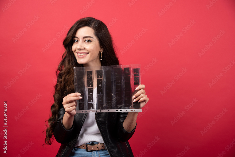 Young woman holding a file with a photo tape on a red background Young woman holding a file with a photo tape on a red background
