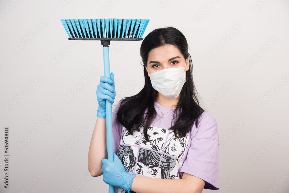 Woman with medical facemask holding broom on white background Woman with medical facemask holding broom on white background