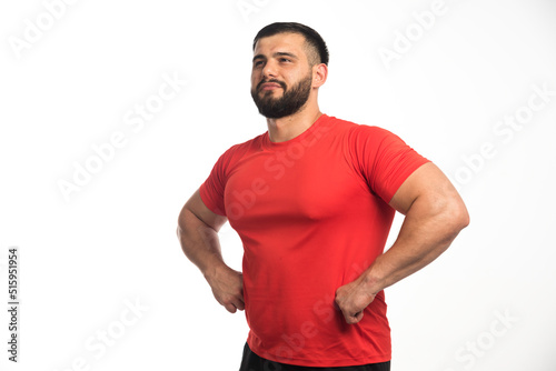 Sportive man in red shirt demonstrating his arm muscles and looks confident