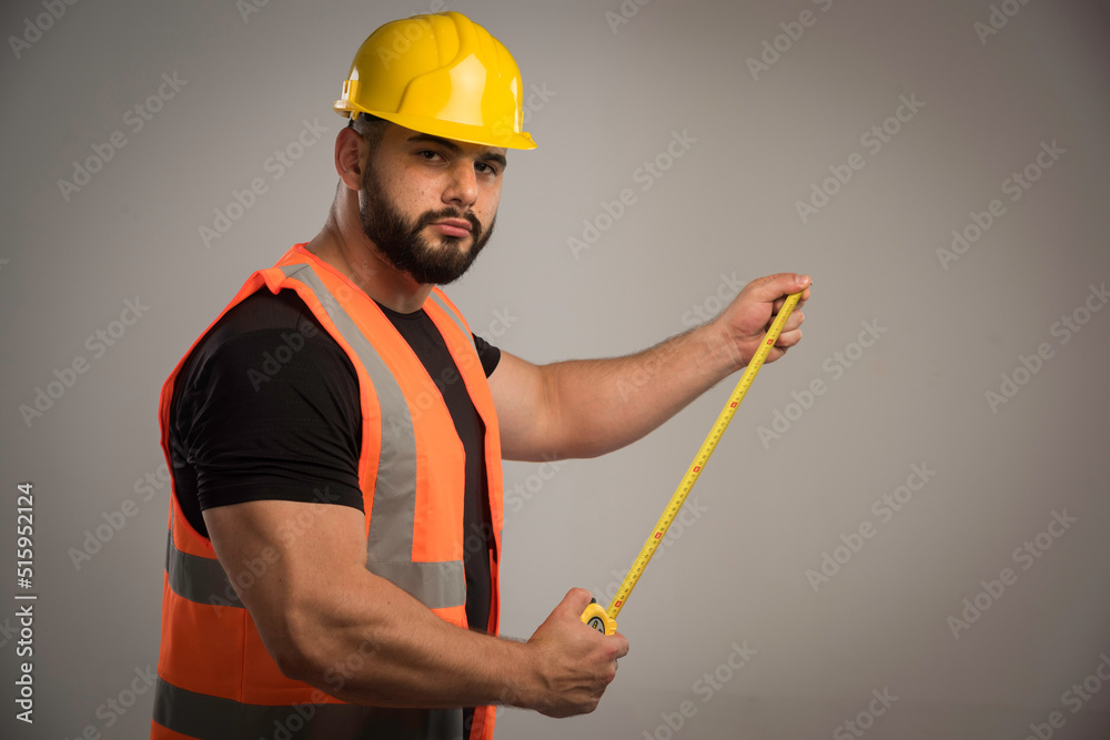 Engineer in orange uniform and yellow helmet using ruler Engineer in orange uniform and yellow helmet using ruler