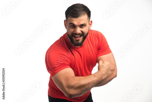Sportive man in red shirt demonstrating his arm muscles