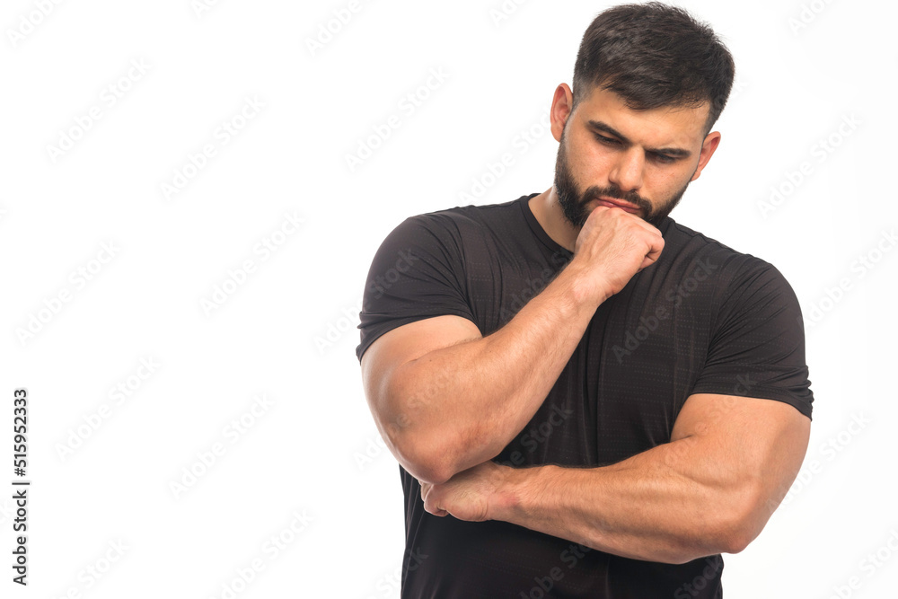 Sportive man in black shirt showing his fists and takes thinking position Sportive man in black shirt showing his fists and takes thinking position
