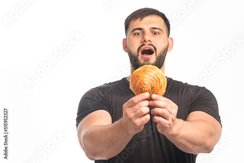 Sportive man in black shirt showing doughnut and his appetite
