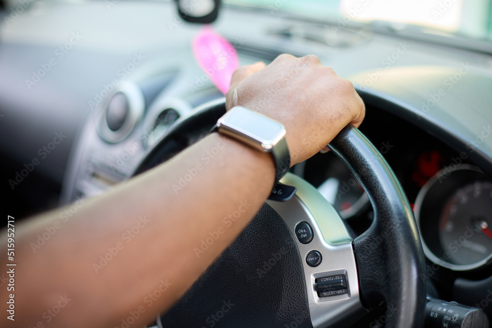 The right hand of a black man on the steering wheel of a car. An African man in a smart watch drives a vehicle