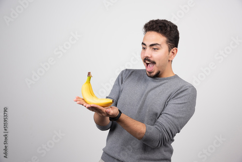 Young man looking at banana on gray background