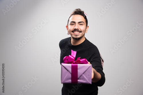 A young man holding a gift box over a gray wall