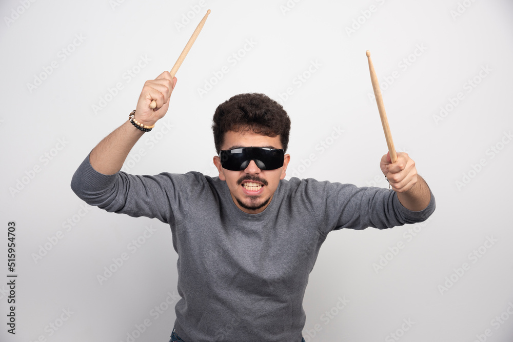 A drummer in black sunglasses holding drum sticks and looks very energic