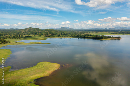 A valley with a lake and tropical vegetation against a blue sky and clouds. Sorabora lake, Sri Lanka.