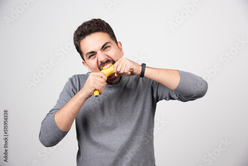 A young man eating a banana over a white wall