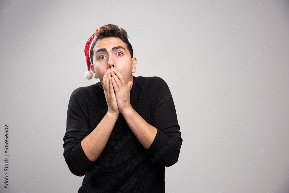 A young man in Santa Claus red hat covering his mouth with hands
