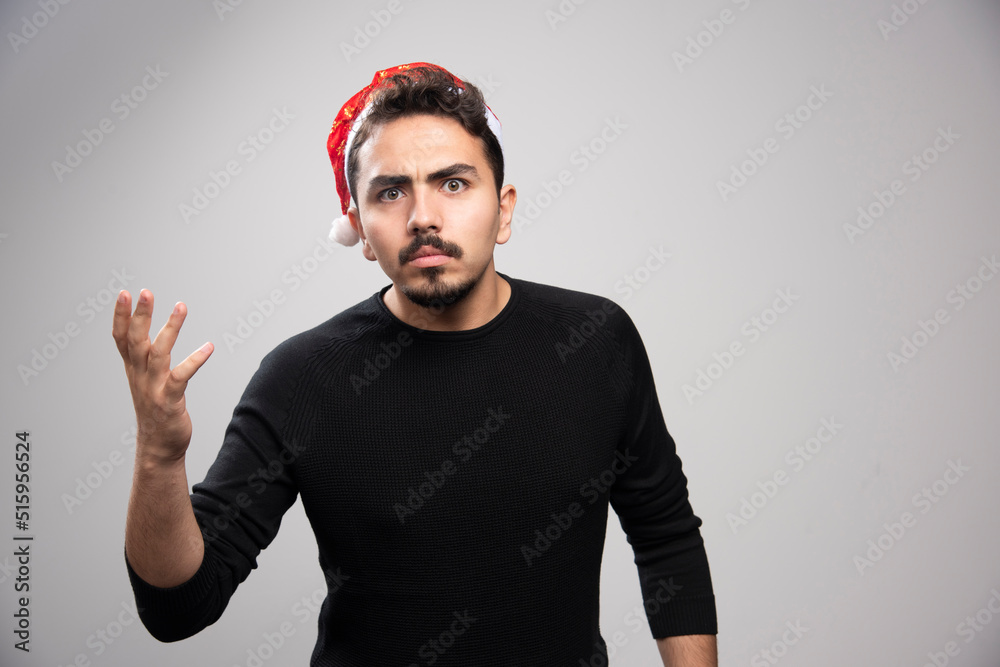 Naklejka premium Disgruntled man wearing Santa Claus red hat over a gray wall
